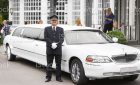 A proud chauffeur standing beside a white stretch limousine